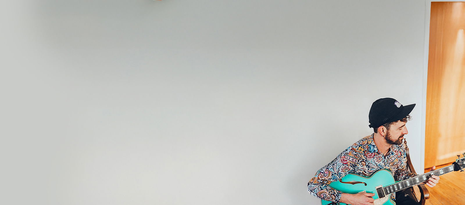 Cloudchord playing an acoustic guitar in front of a grey wall