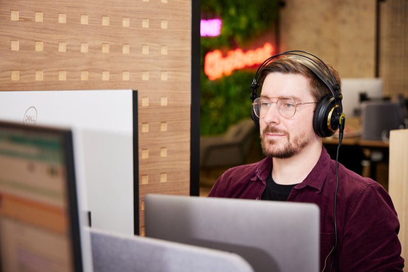 A creator wearing headphones editing at a desk with two monitors.