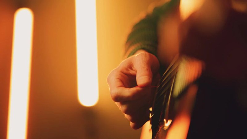 A close-up of a hand playing an acoustic guitar in a warmly lit studio.