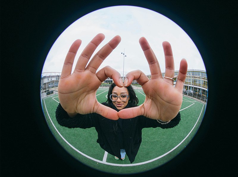 A creator framing a heart shape with their hands, shot through a fisheye lens.
