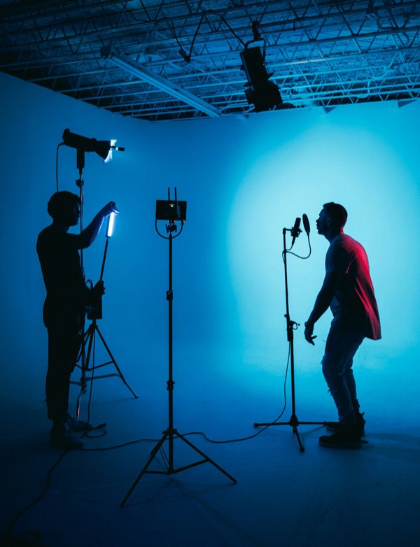 Two people setting up lights and a camera on a blue-lit film set.