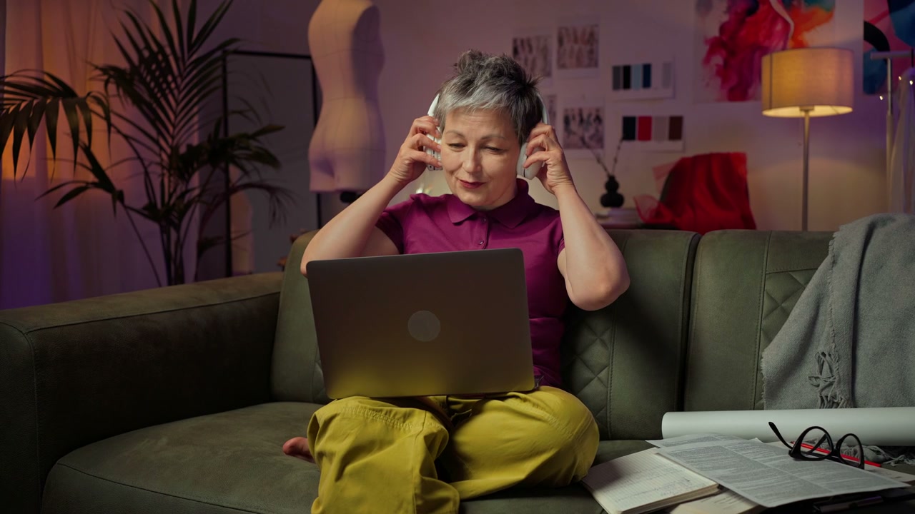 Senior Woman Puts On Headphones Using Laptop
