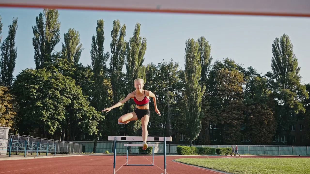 Athlete Running Hurdles on Track