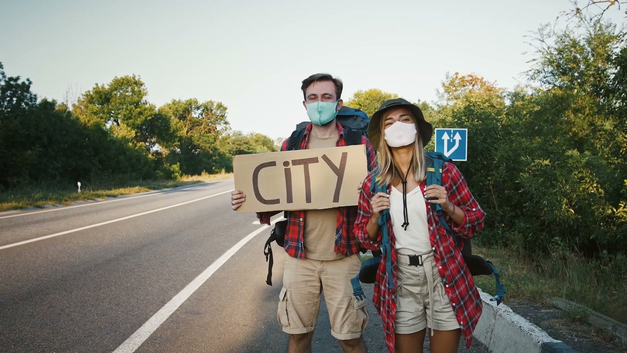 Hitchhiking Couple Holding City Sign by Roadside