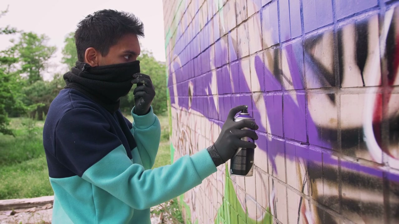 Masked Man Spray Painting Graffiti on Wall