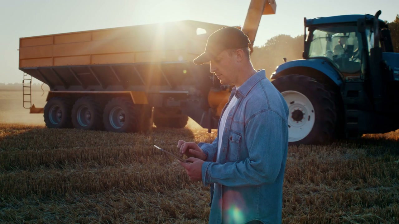 Farmer Using Tablet on Harvest Field at Sunset