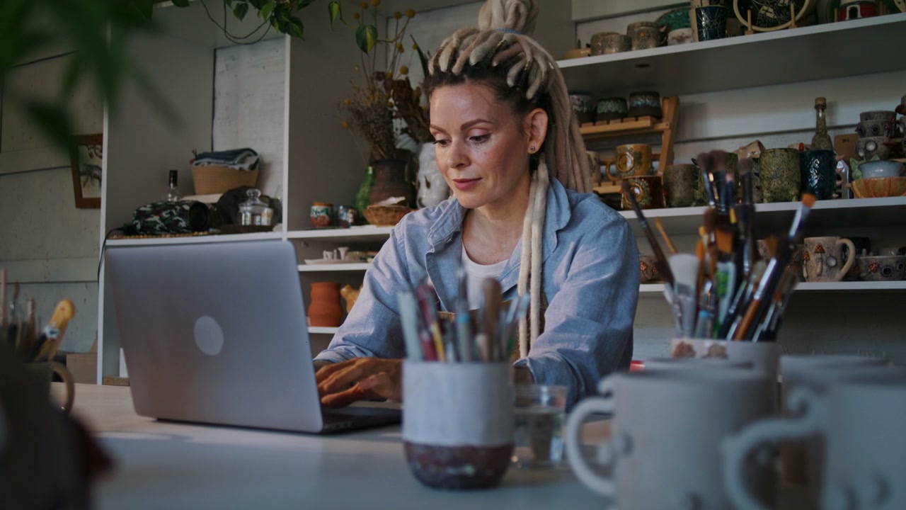 Woman Typing on Laptop in Ceramic Studio