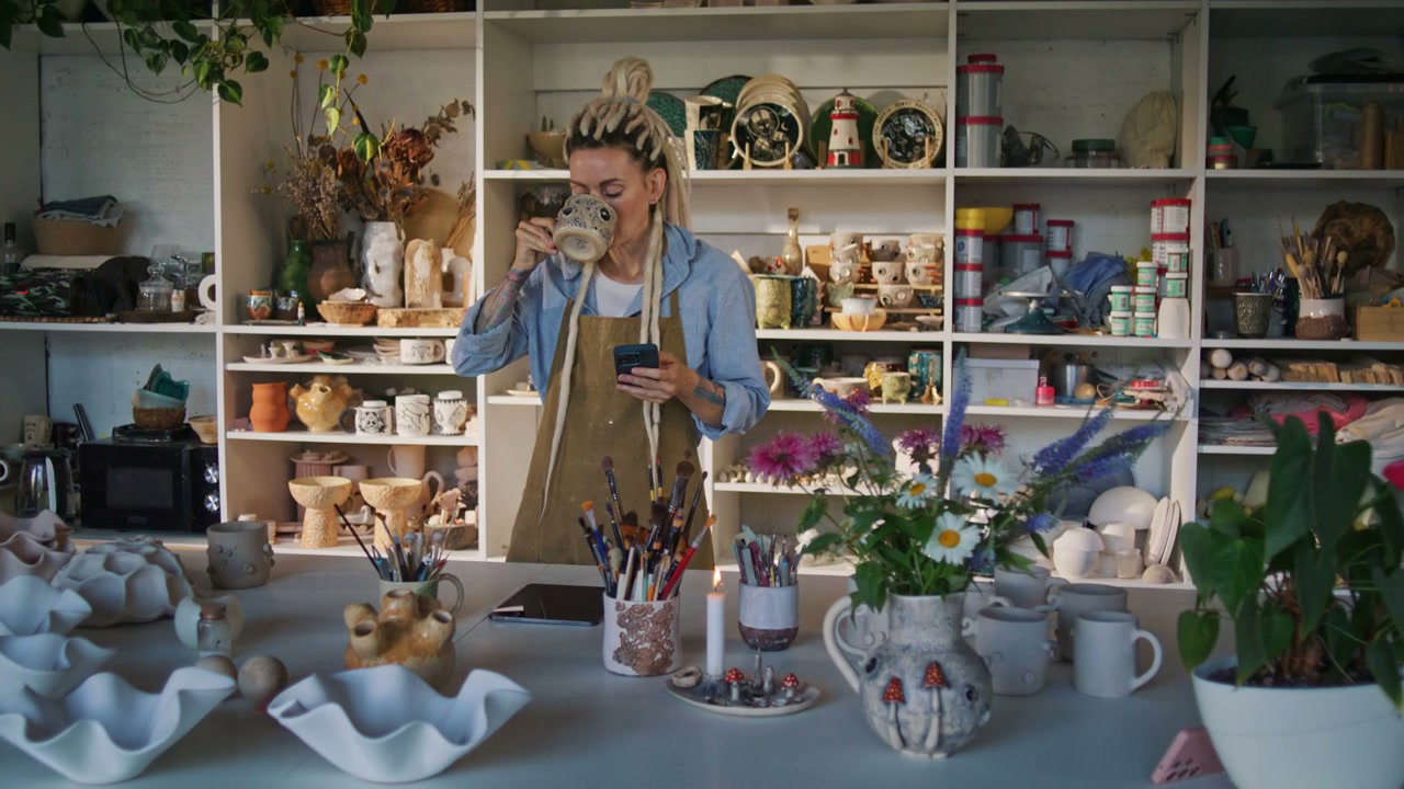 Female Artist Using Phone in Pottery Studio