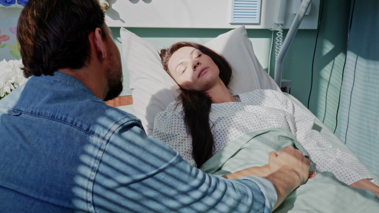 Man Holds Hand of Woman in Hospital Bed