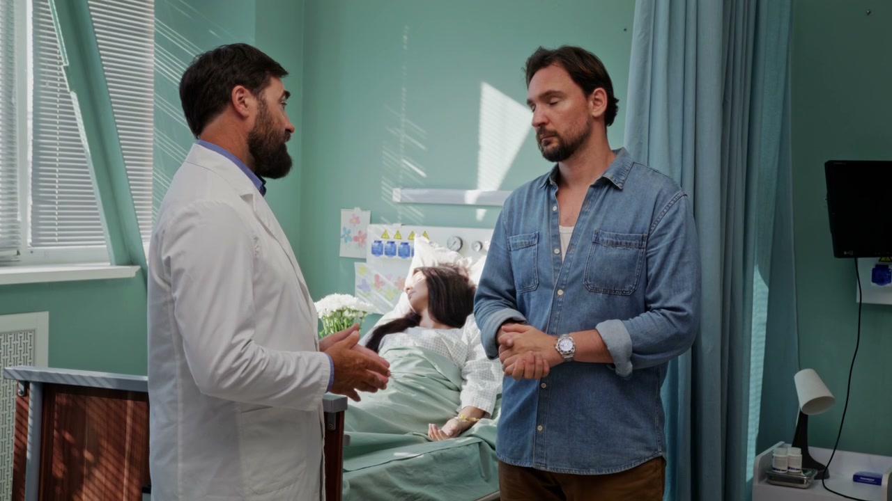 Doctor Talks to Concerned Man in Hospital Room