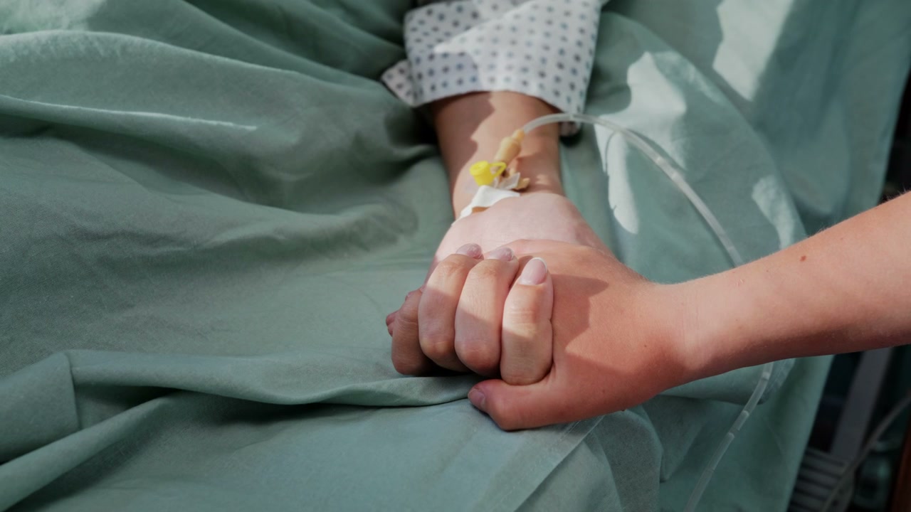 Hand Holding Patient's Hand in Hospital Bed