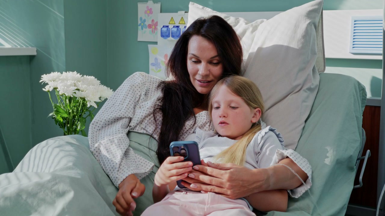 Mother and Daughter Use Phone in Hospital Bed