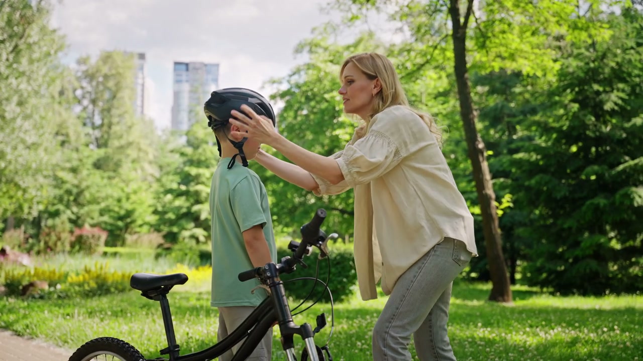 Woman Fastens Helmet on Boy Next to Bicycle