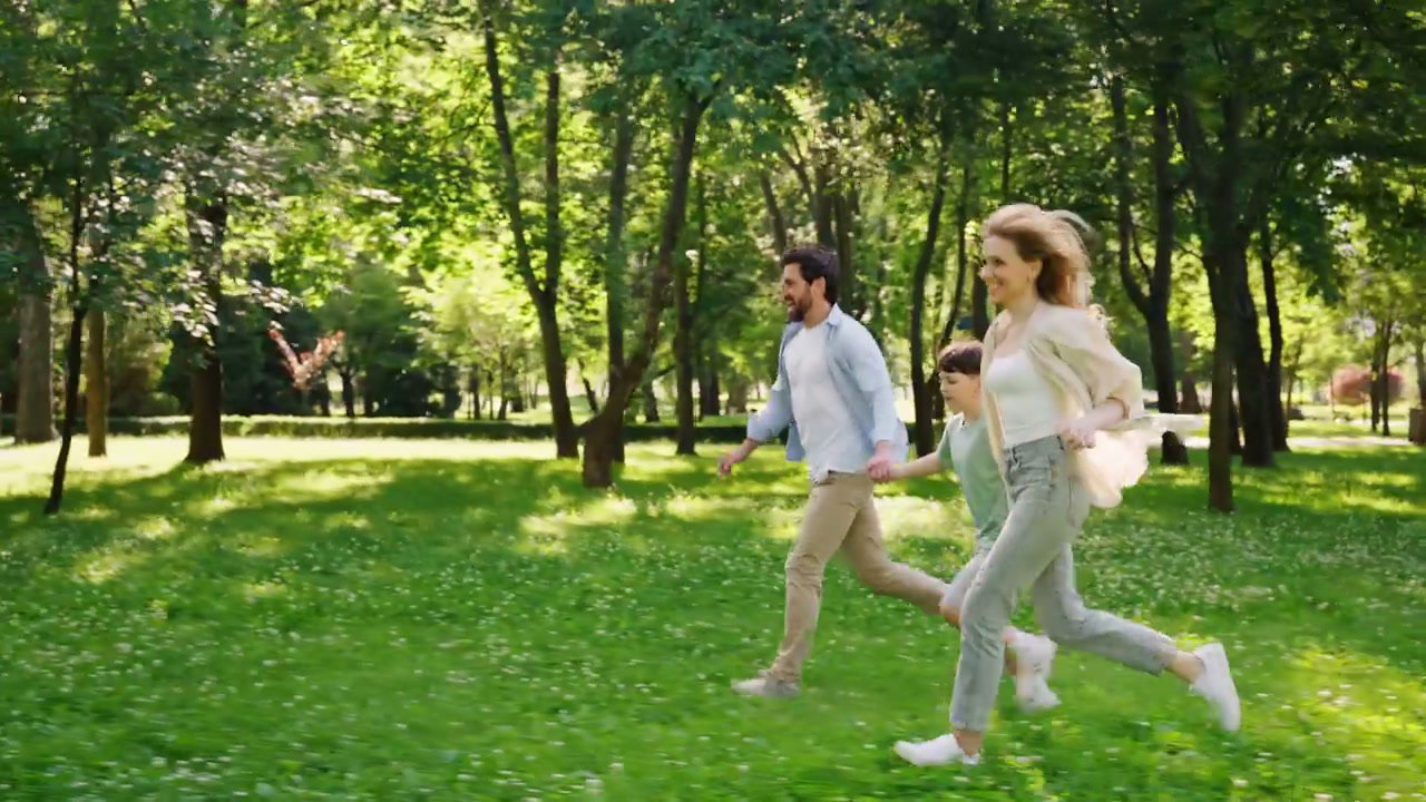 Family Running Hand in Hand Through Park Grass