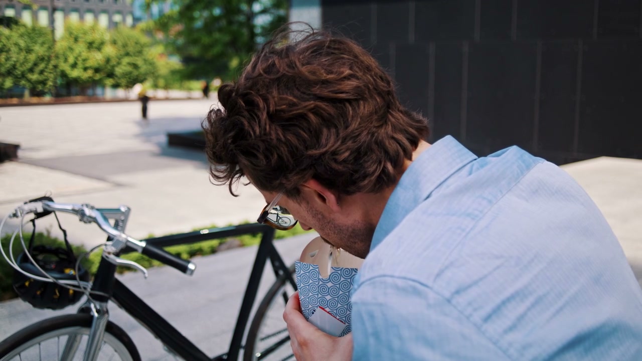 Man Eating Takeaway Noodles Next to Bike