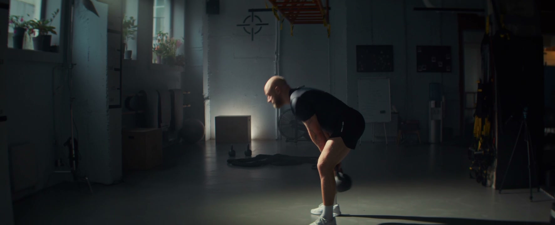 Bald Man Doing Kettlebell Swings in a Gym