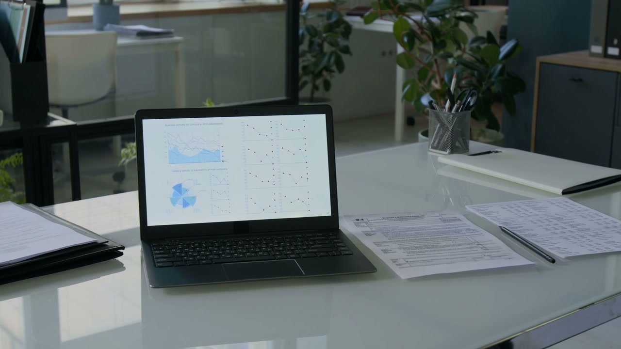 Laptop With Financial Charts On Office Desk
