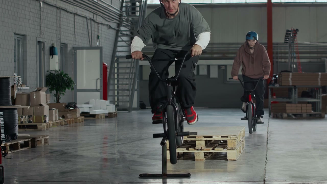 Two BMX Riders Performing Tricks in Hangar