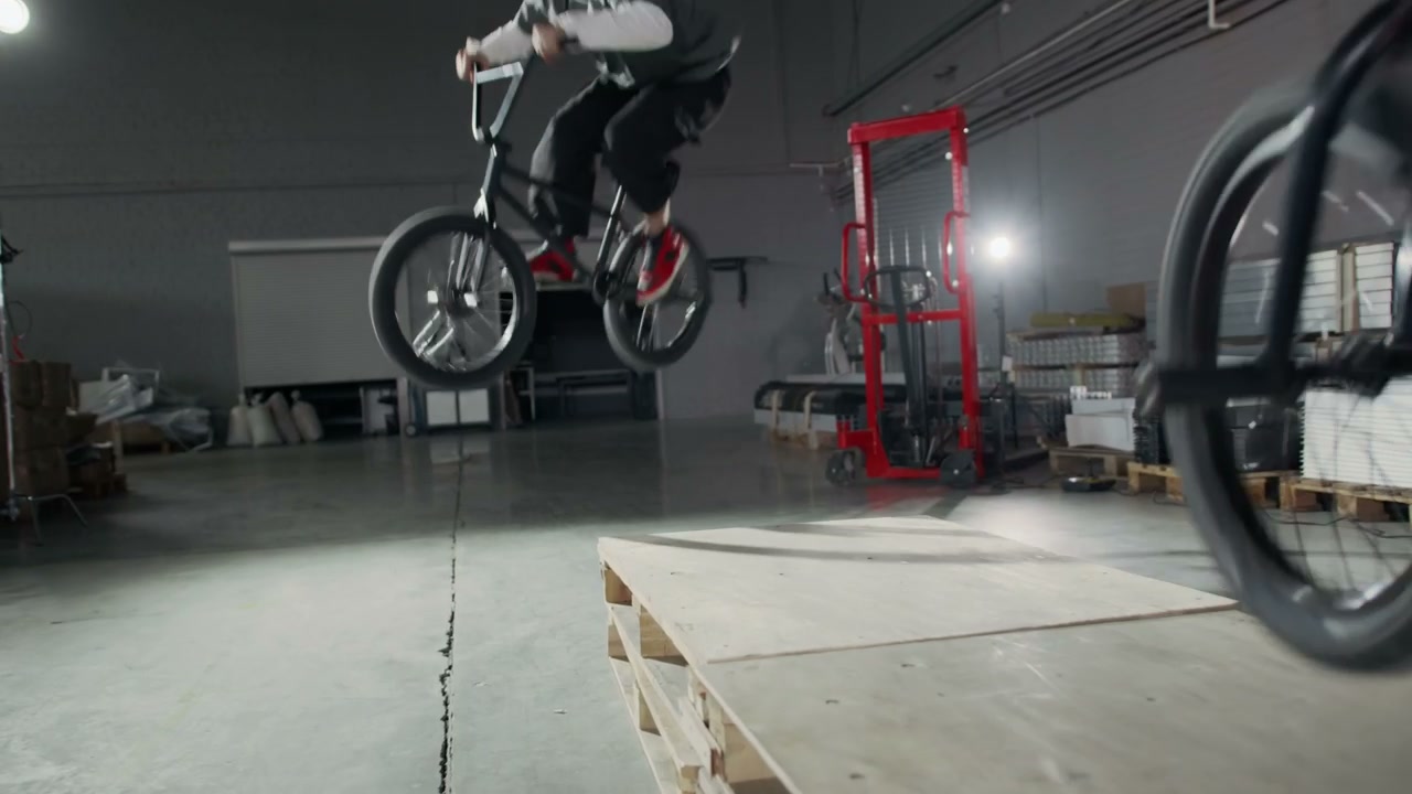 BMX Riders Jumping Over Pallets in Hangar