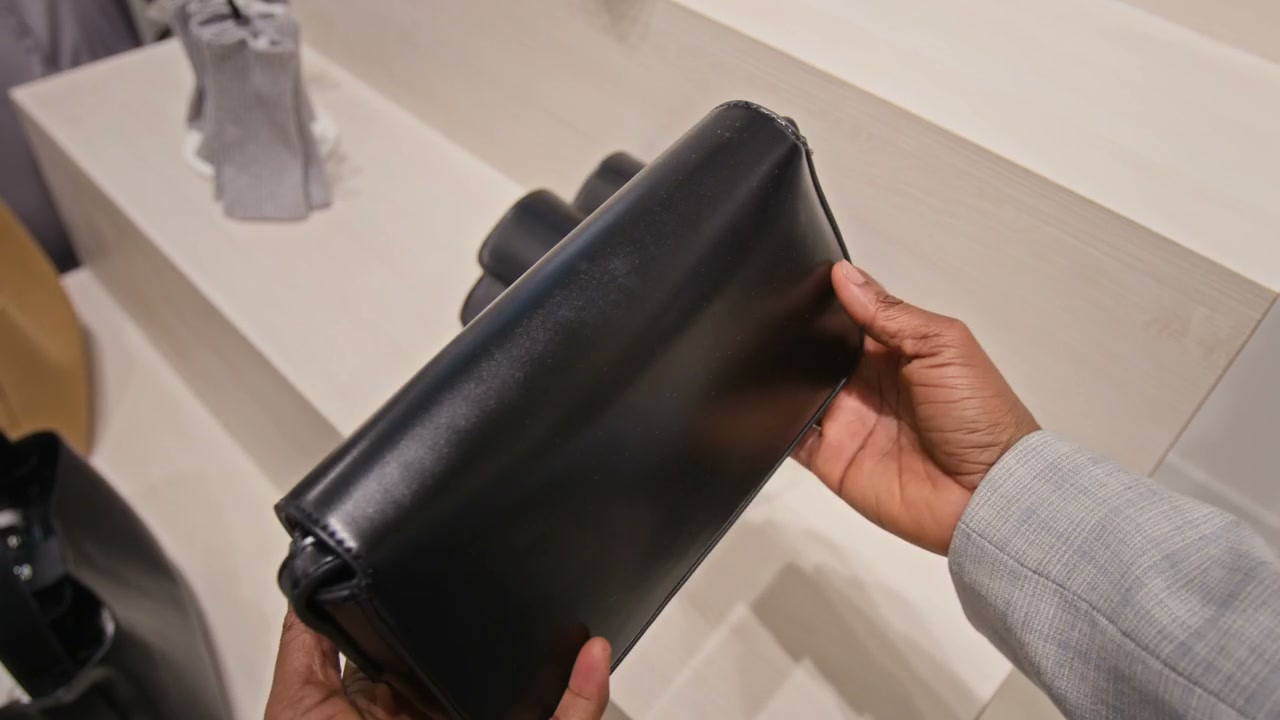 Hands Examining Black Clutch Bag in Boutique