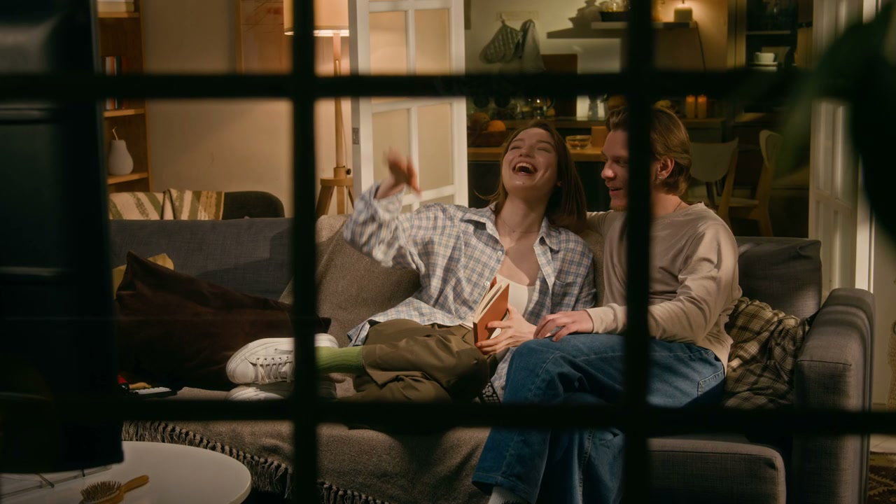 Happy Couple Laughing On Couch Through Window