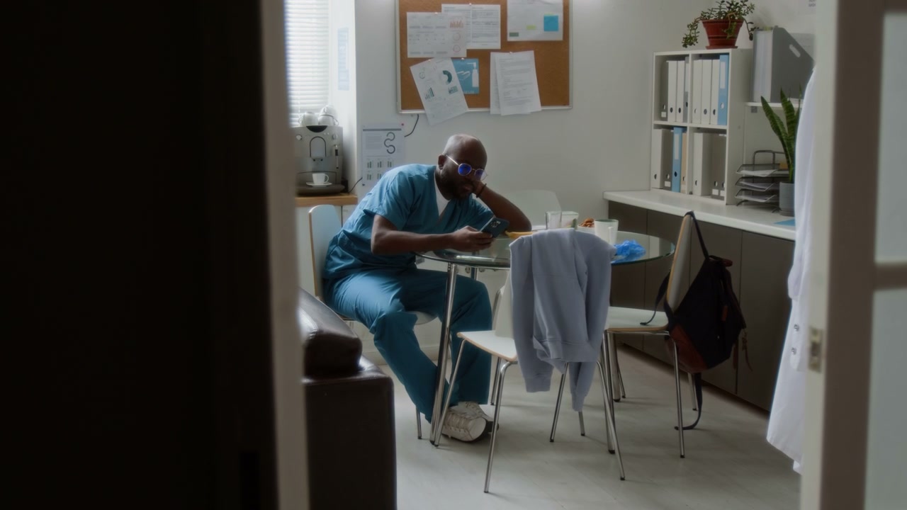 Male Clinician Using Smartphone in Break Room
