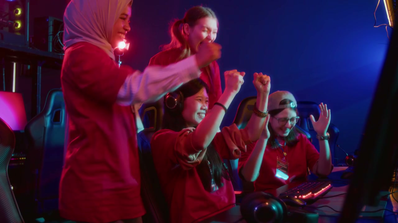 Diverse Girls Cheering on Asian Teammate Playing Video Game in Cyberclub