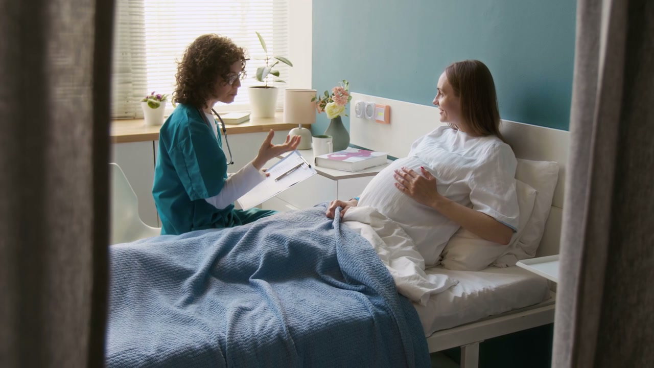 Midwife Consulting Pregnant Woman in Hospital Bed