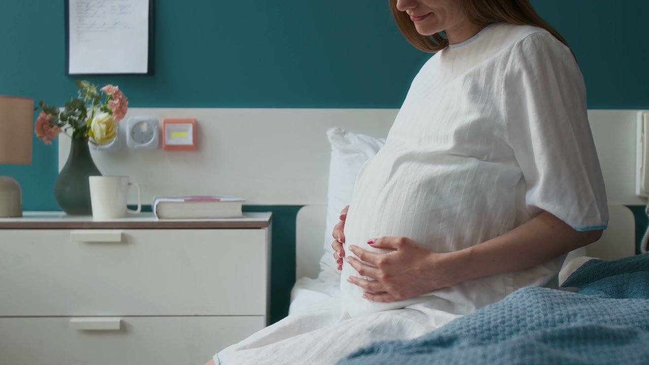 Pregnant Woman Caressing Belly in Hospital Room