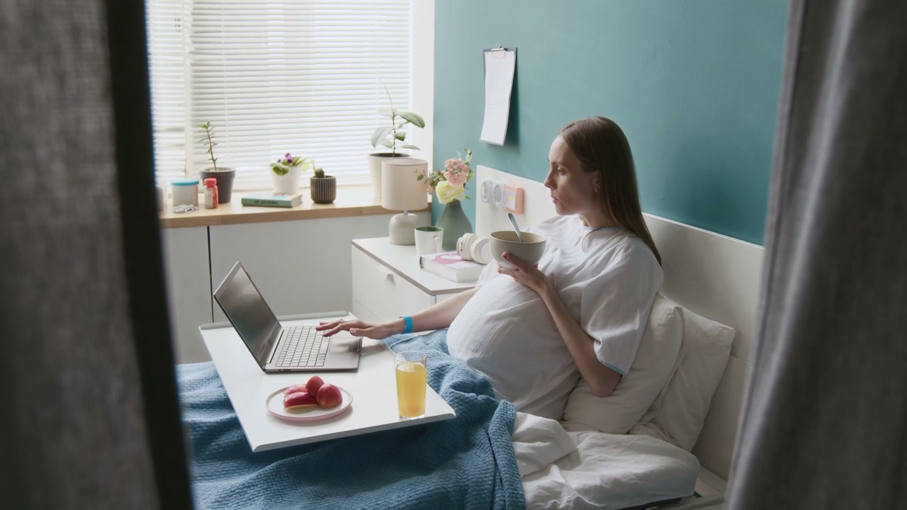 Pregnant Woman Using Laptop in Hospital Bed