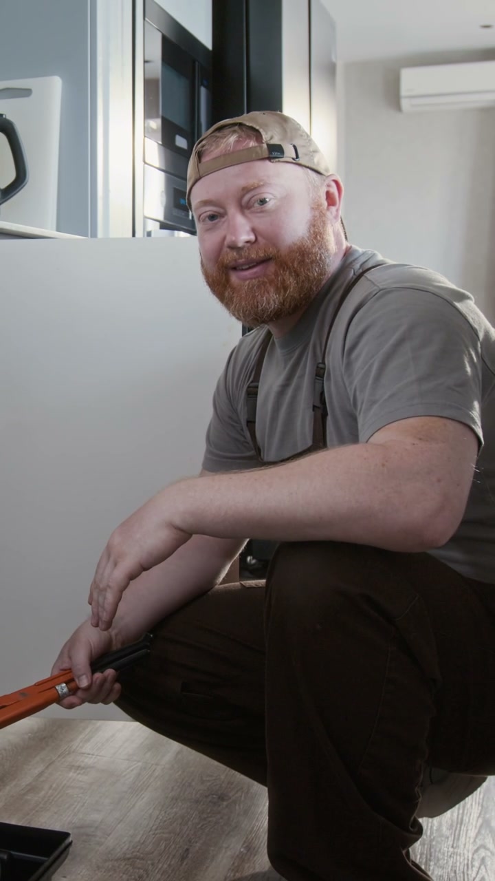 Smiling Plumber Holding Wrench in Kitchen