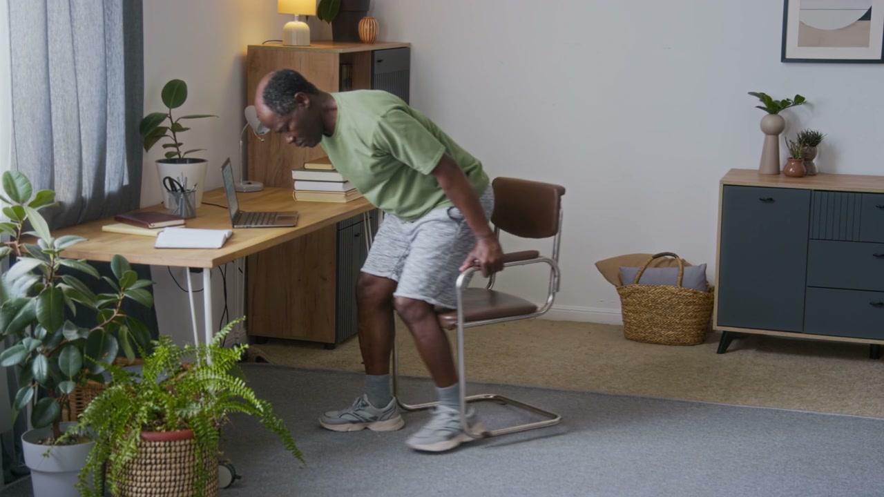 Senior Man Stretching at Desk in Home Office