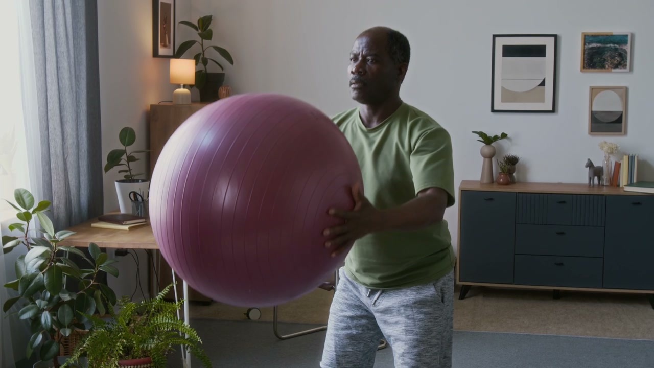 Senior Man Squatting With Exercise Ball At Home