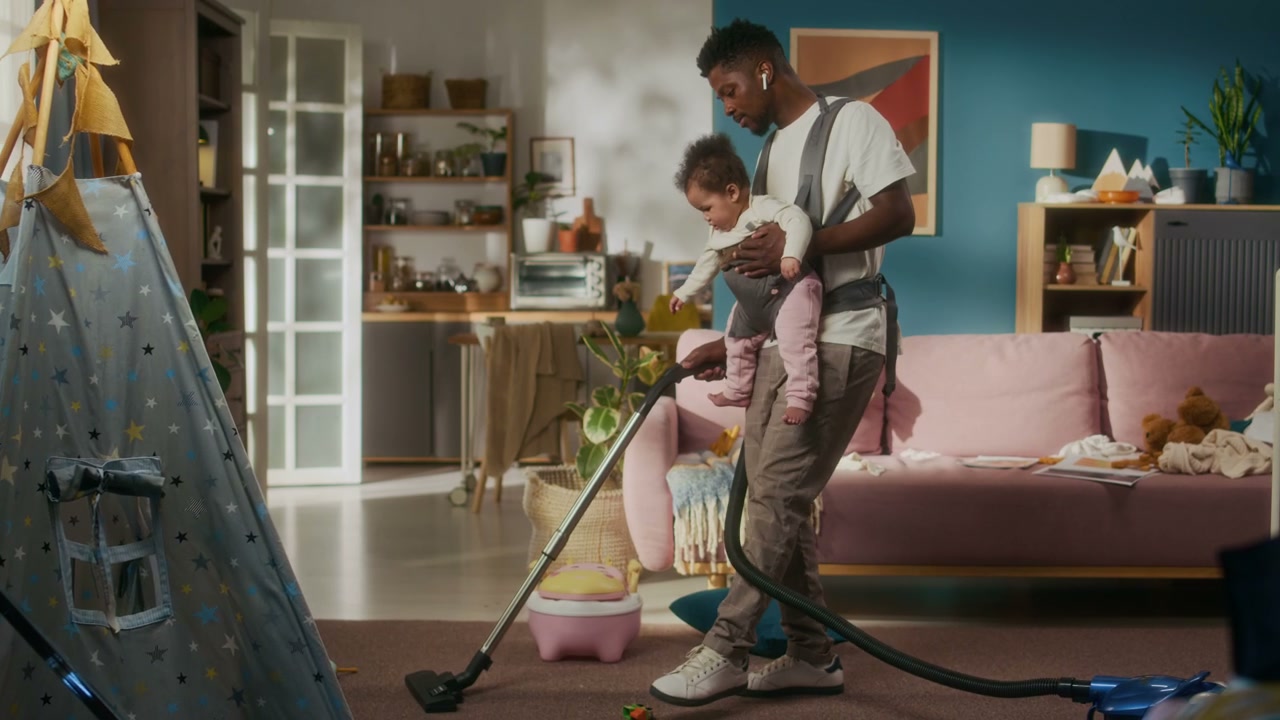 Dad Vacuuming Living Room While Carrying Baby