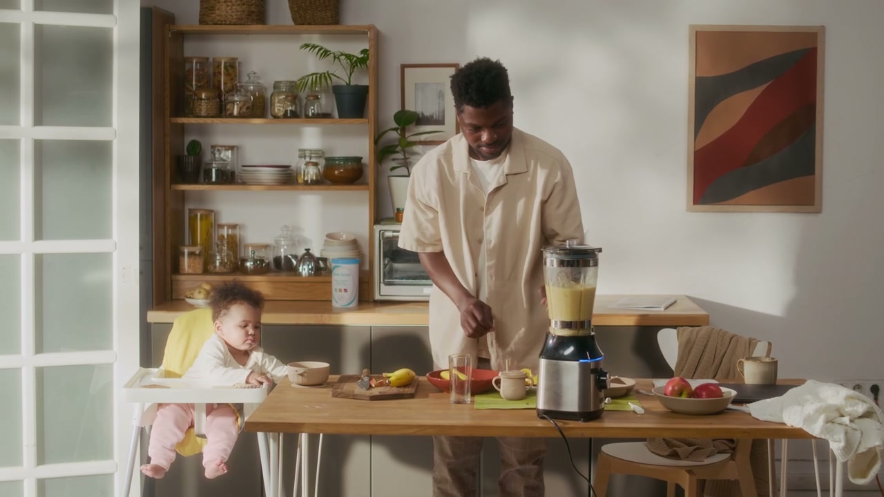 Black Dad Prepares Smoothie with Baby in High Chair