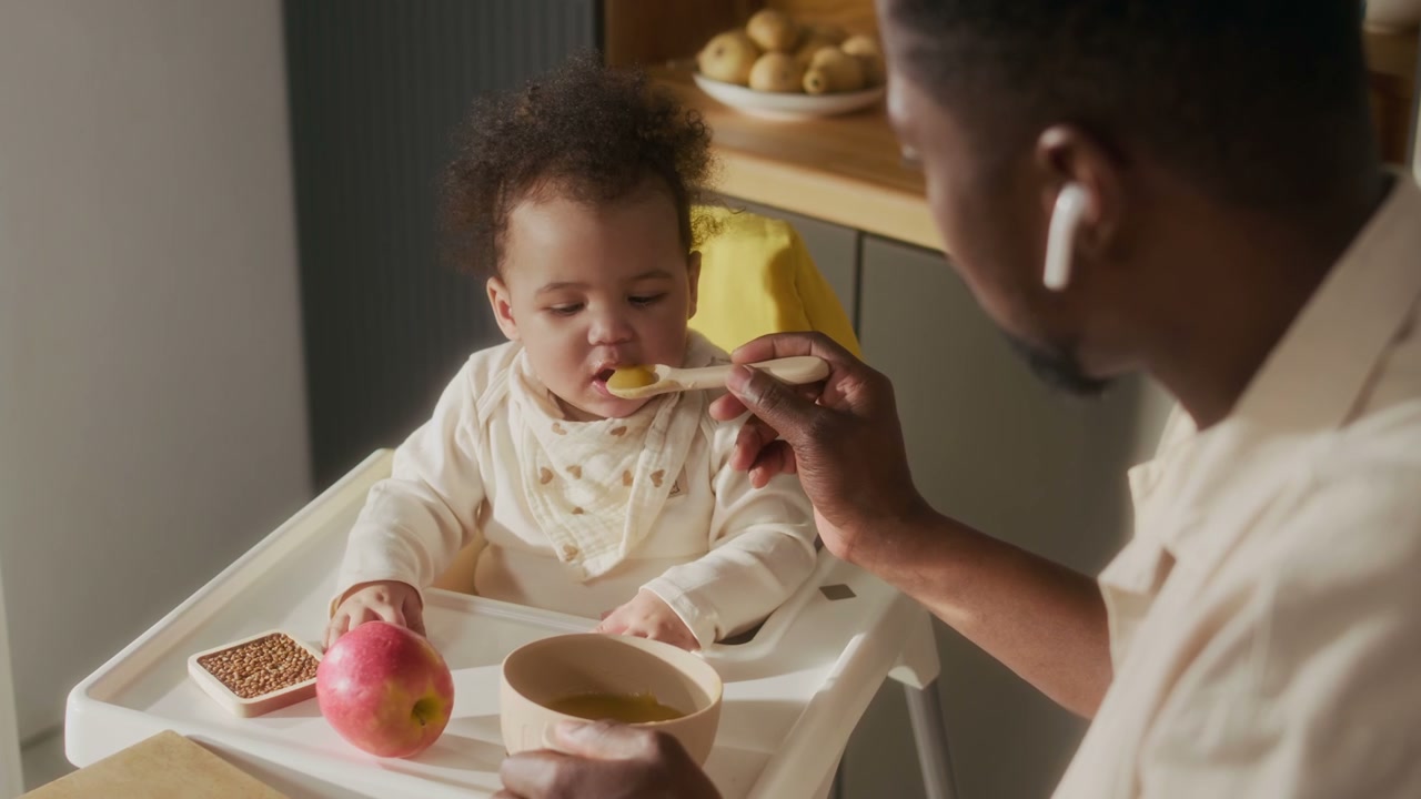 Father Feeding Baby Solid Food in High Chair