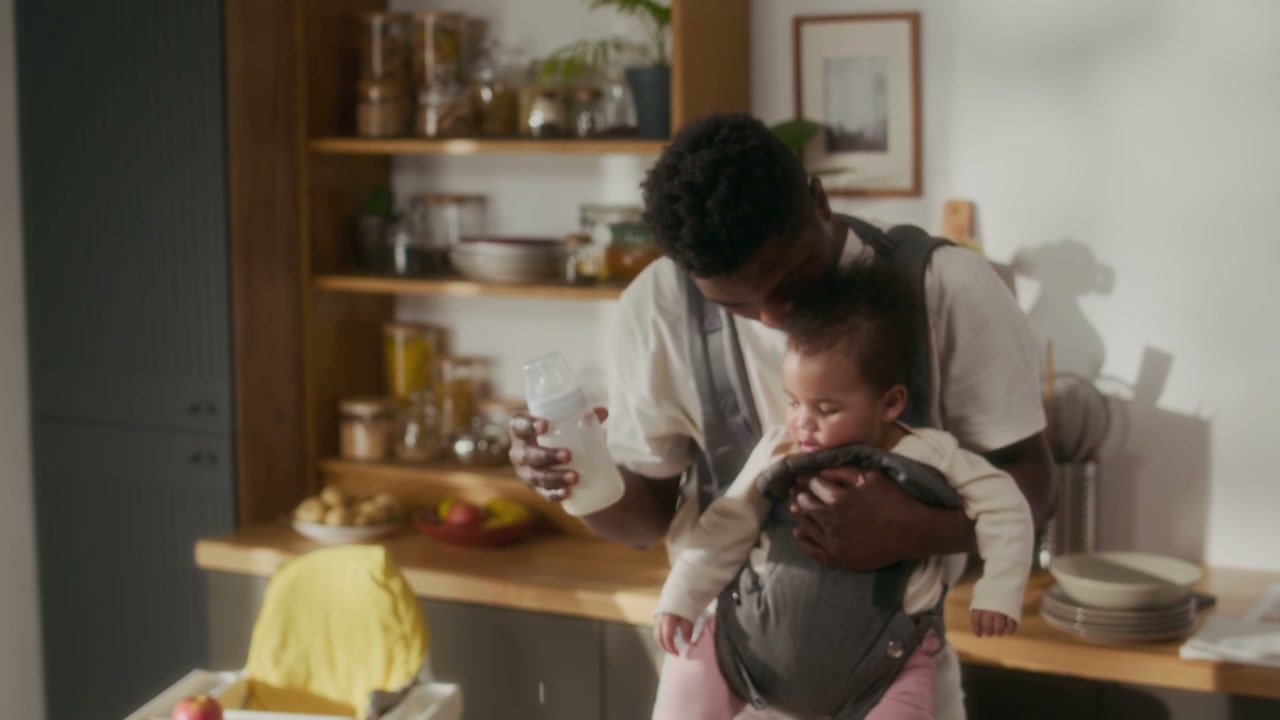 Father Prepares Baby Bottle with Child in Carrier