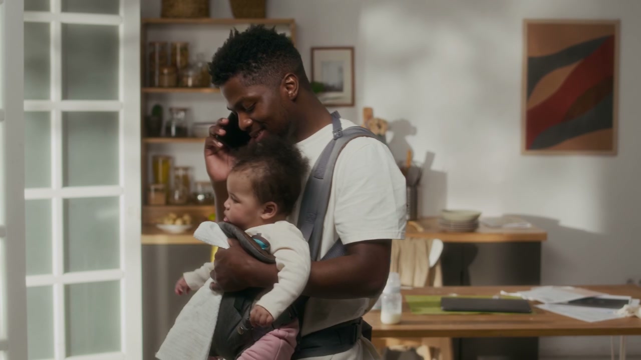 Dad Talking on Phone While Carrying Baby at Home
