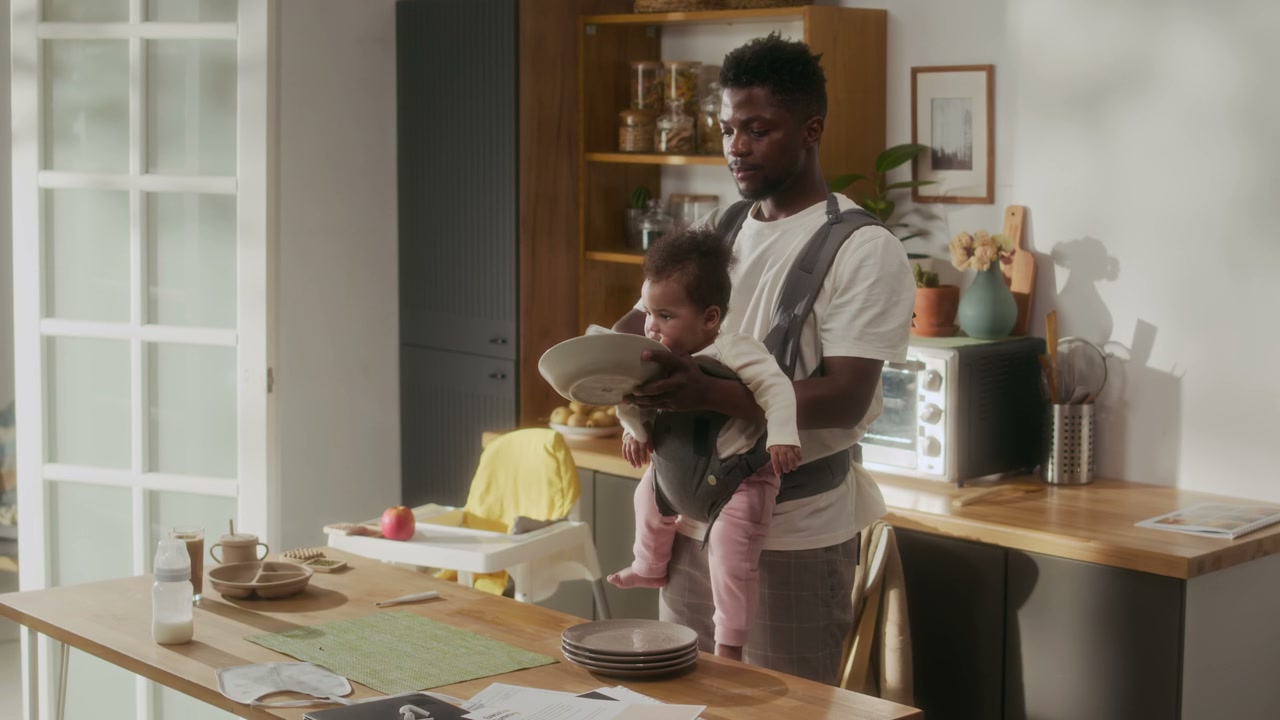 Father Carrying Baby While Cleaning Dishes