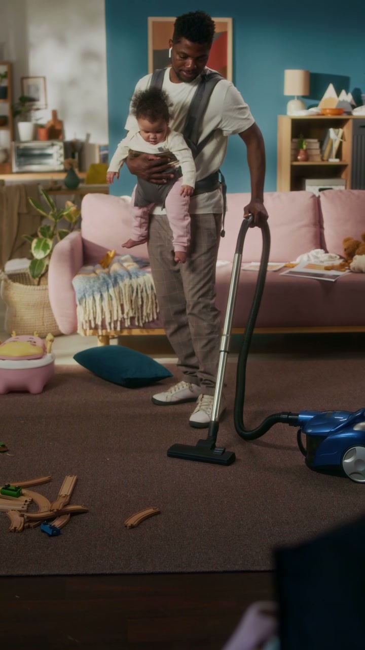Father with Baby in Carrier Vacuuming