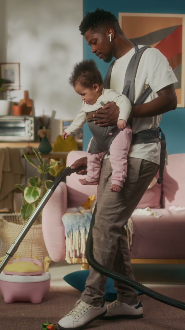 Dad Vacuuming Floor While Babywearing Daughter