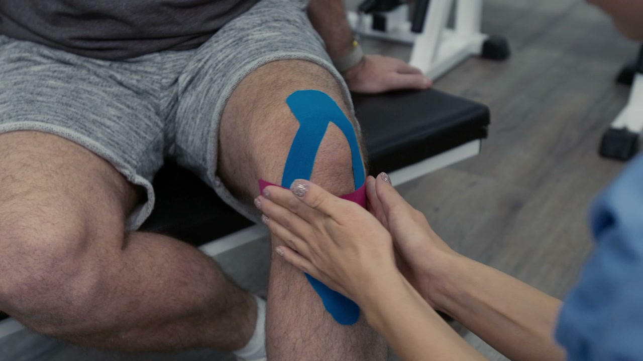 Physiotherapist Applying Kinesiology Tape on Knee