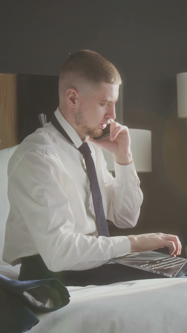 Man Working on Laptop and Phone in Hotel Bed