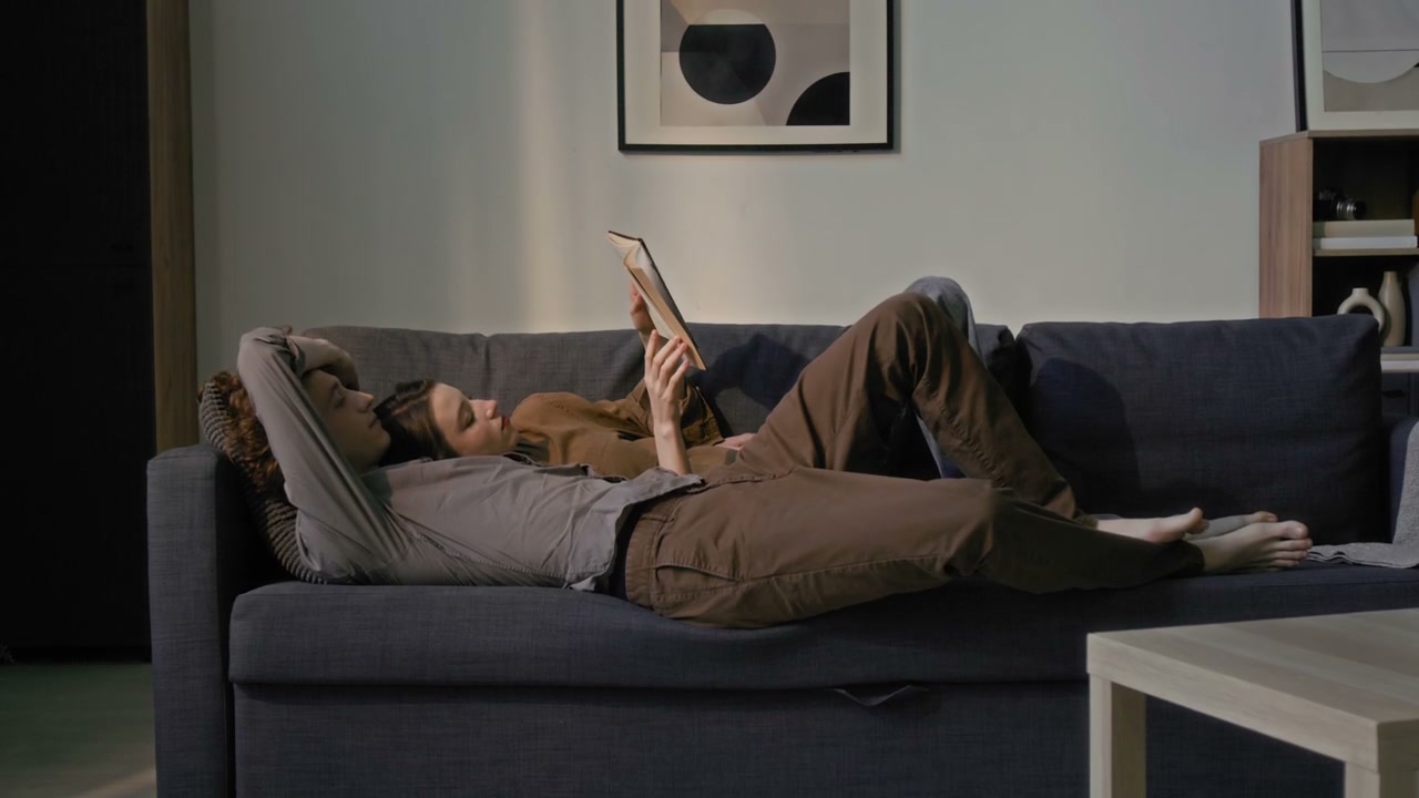 Couple Reading Book on Sofa at Home