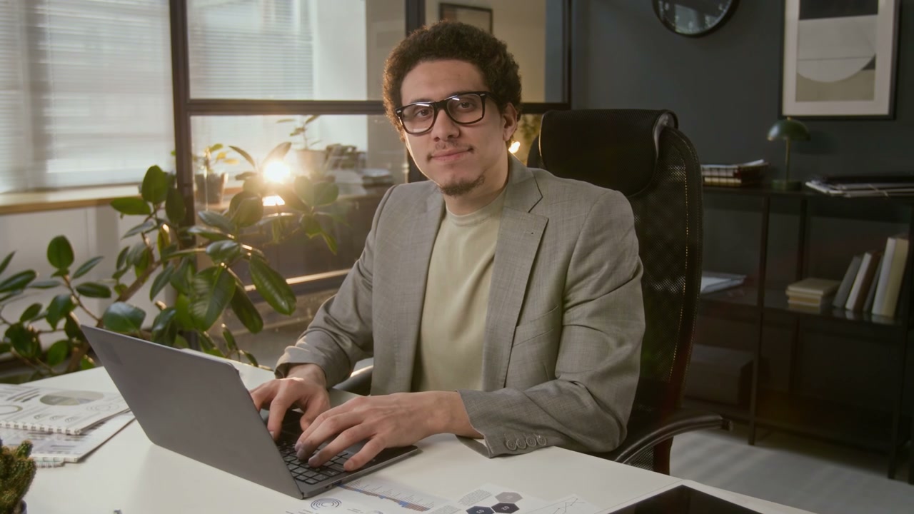 Young Man Smiling and Typing on Laptop in Office