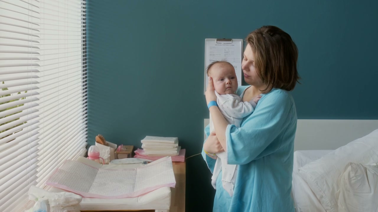 Mother Cuddles Newborn Baby in Hospital Room