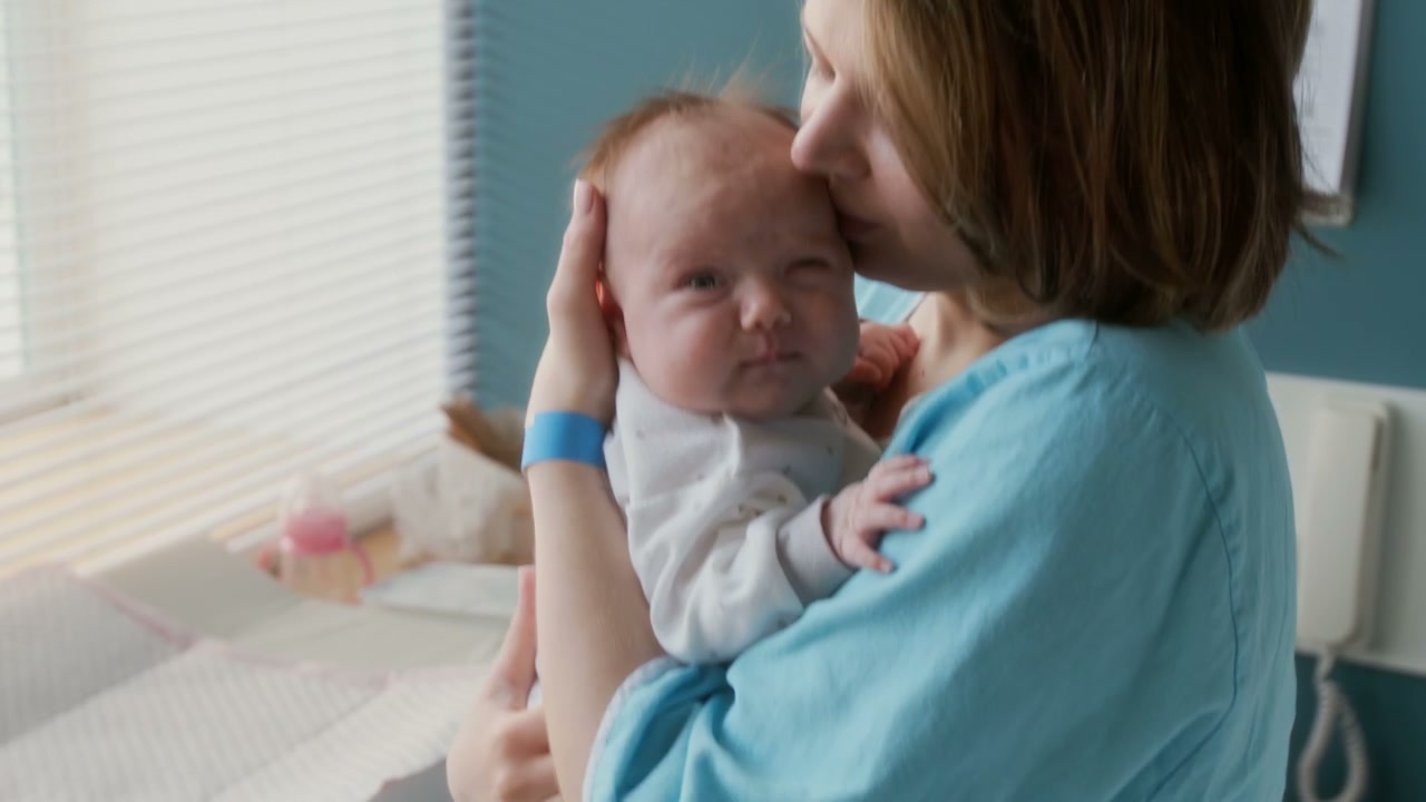 Mother Kisses Newborn Baby in Hospital Room