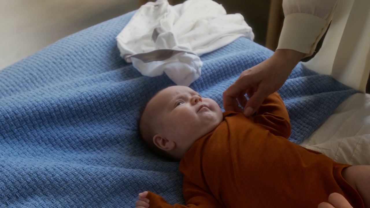 Mother Dressing Newborn Baby on Bed