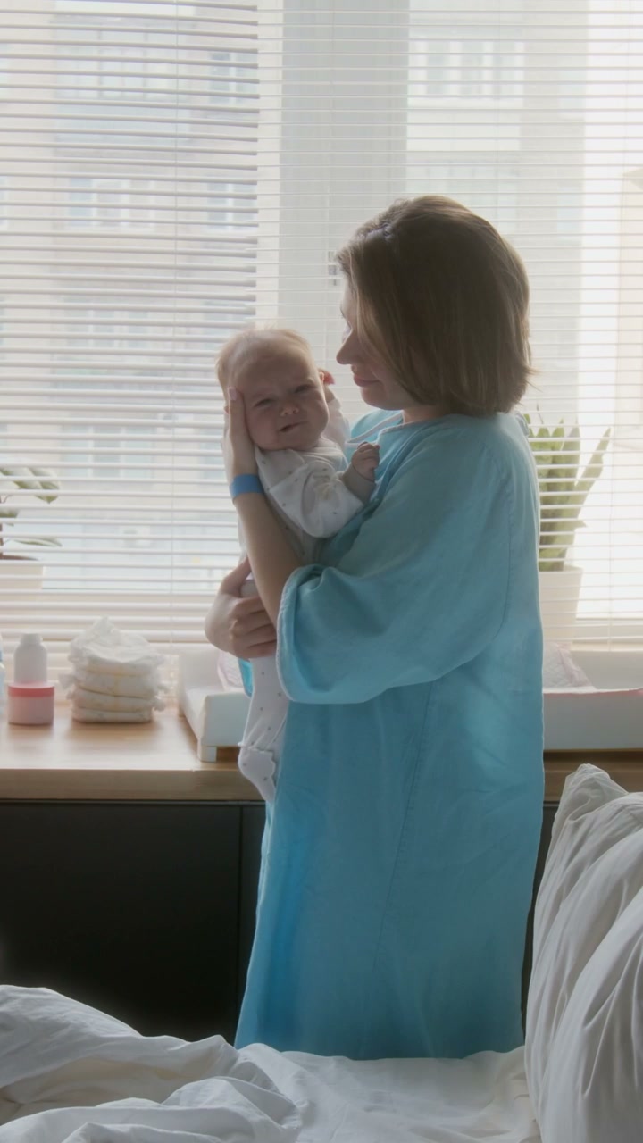 Mother Holding and Kissing Newborn Baby in Hospital