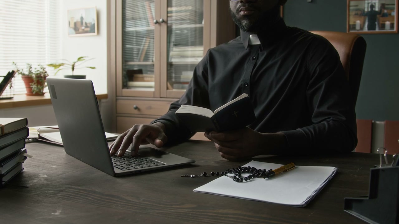 Priest Using Laptop and Holding Holy Book